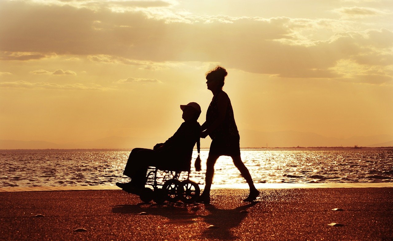 Mujer paseando a un hombre (paciente) en silla de ruedas